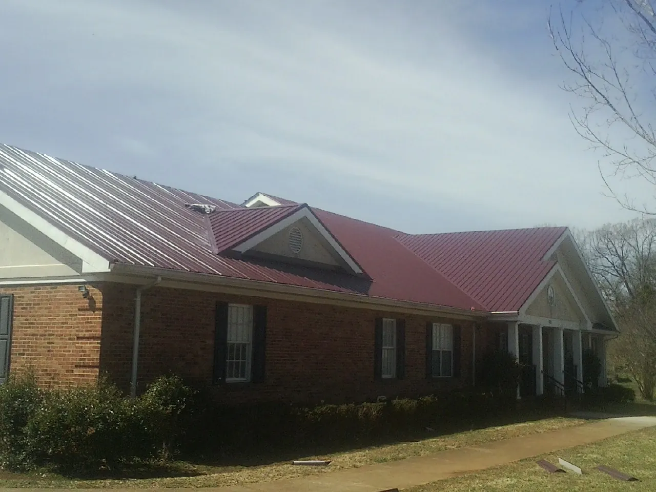 Red metal roof with gabled entries on a long brick building, from a Hail Damage Roof Repair job in Jemez Pueblo