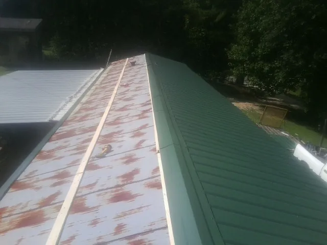 Old rusted panels beside newly installed green metal roofing — Wind Damage Roof Repair by Roofing Brothers in Jemez Pueblo