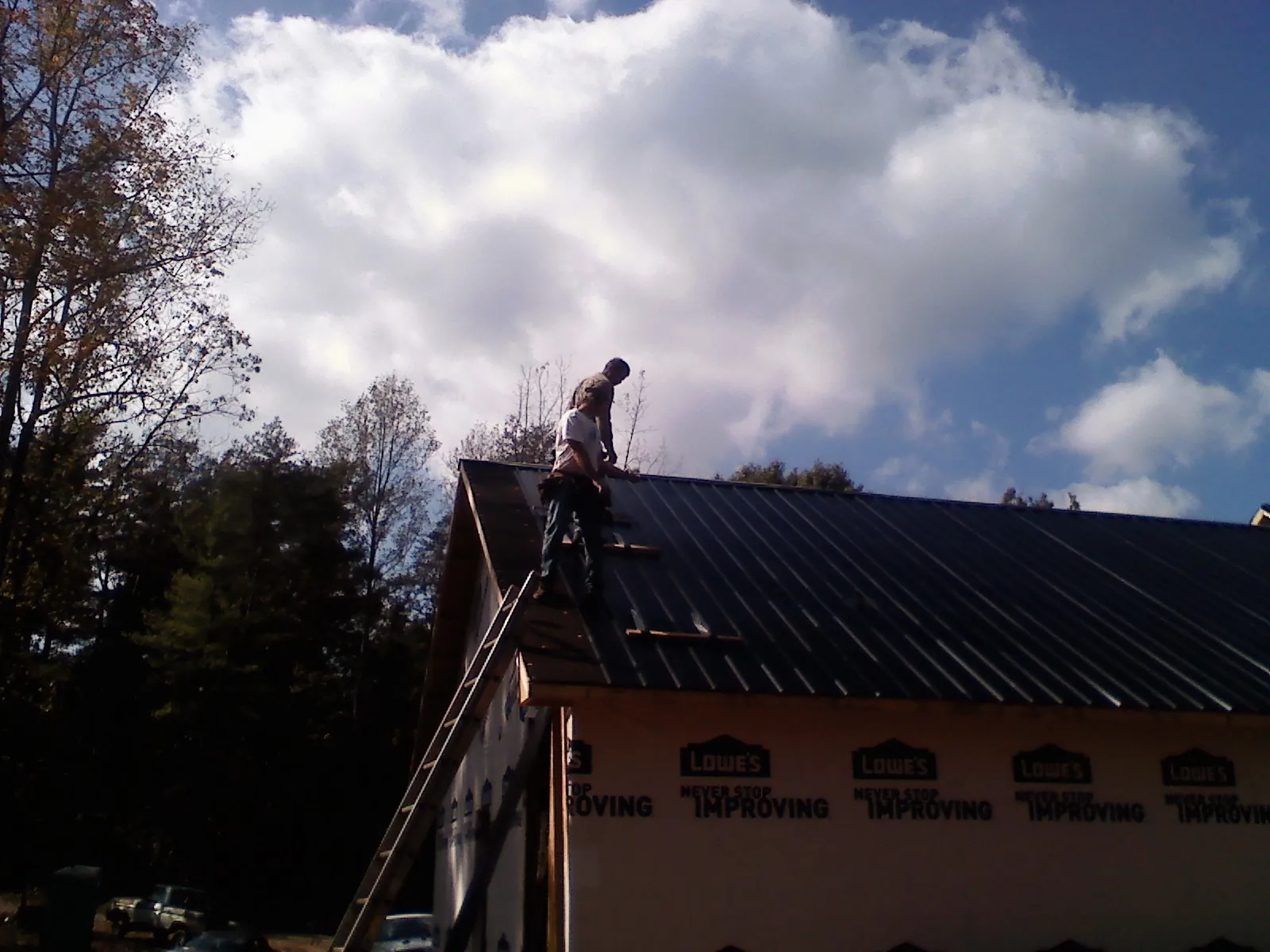 Roofer fastening dark metal panels high against a cloudy sky, from a Roof Inspection job in Jemez Pueblo