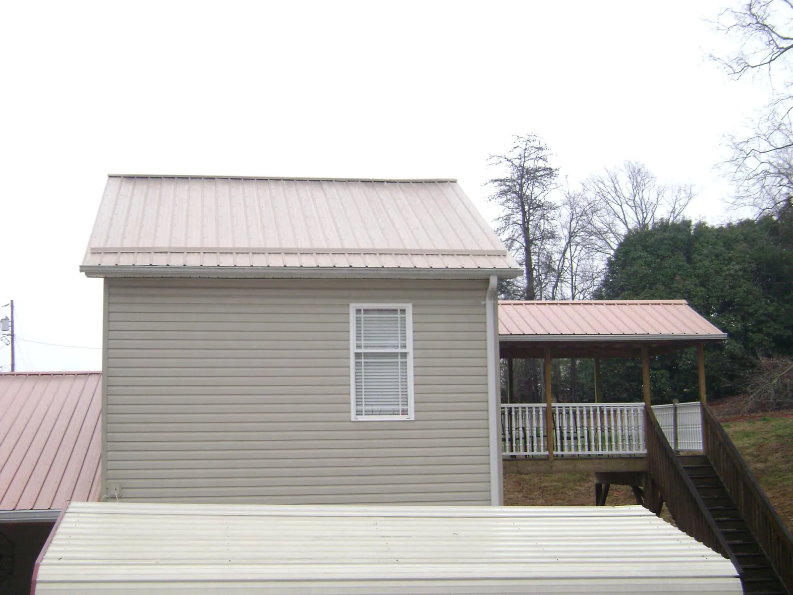 Tan metal roofs on a two story addition and attached porch, from a Roof Replacement job in Jemez Pueblo